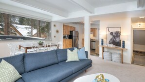 A modern living room with a blue sofa, white coffee table, and a view of the kitchen and dining area. - Private East Vail Home on Bus Rte, 5187GC (Vail)