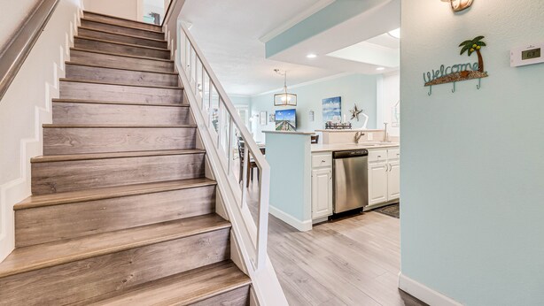 A staircase leading to a kitchen area with a light blue wall, a welcome sign, and a pendant light. - Bayfront Kontiki 3 Bedroom Condo by RedAwning (Rockport)