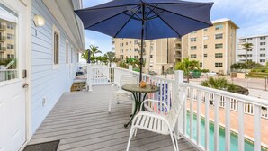 A wooden deck with a table and chairs, a large umbrella, and a pool in the background.
