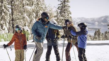 A group of skiers on a snowy slope with trees and a lake in the background.