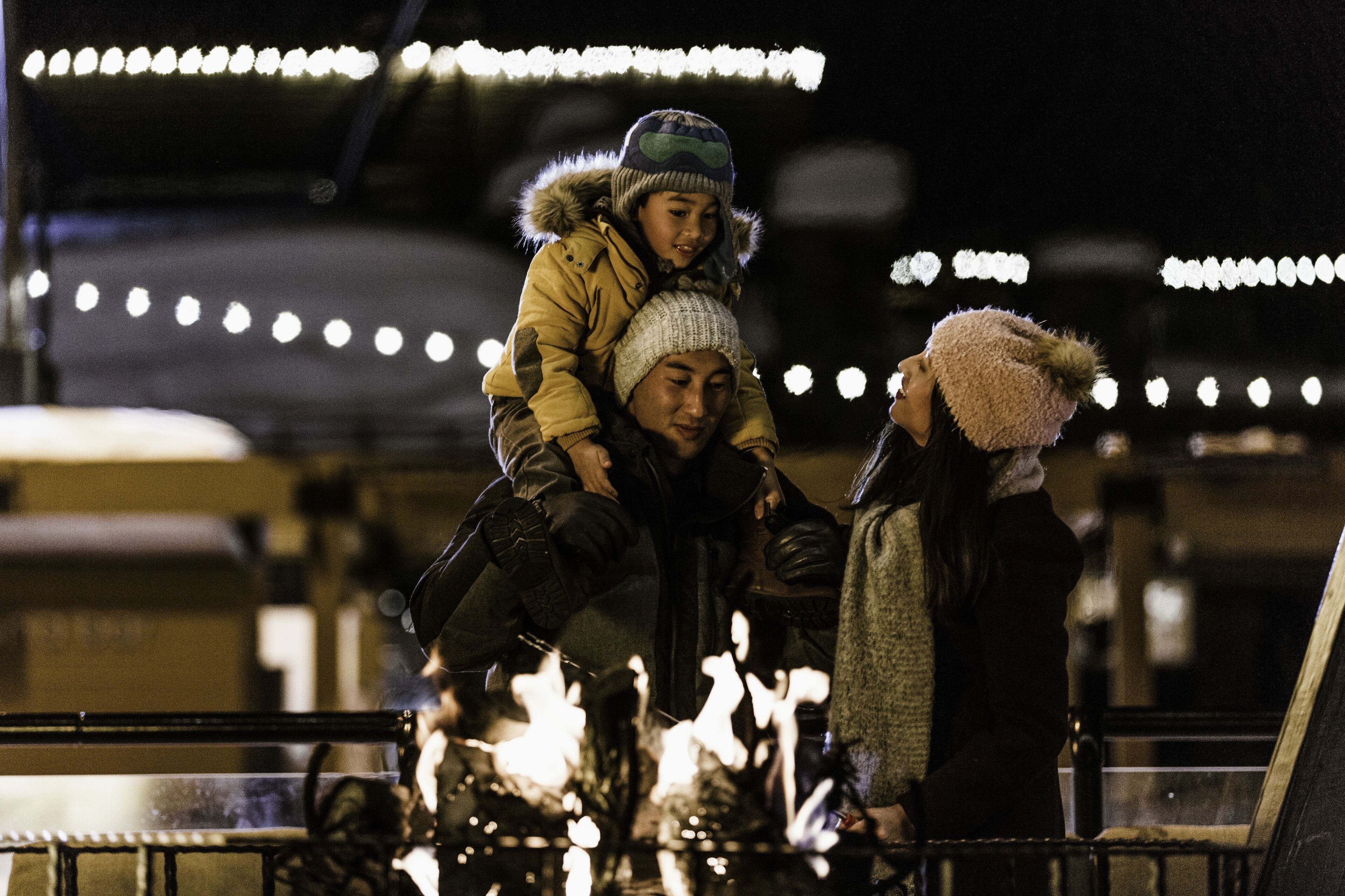 A nighttime scene with a person carrying another on their shoulders, a railing, and lights in the background.