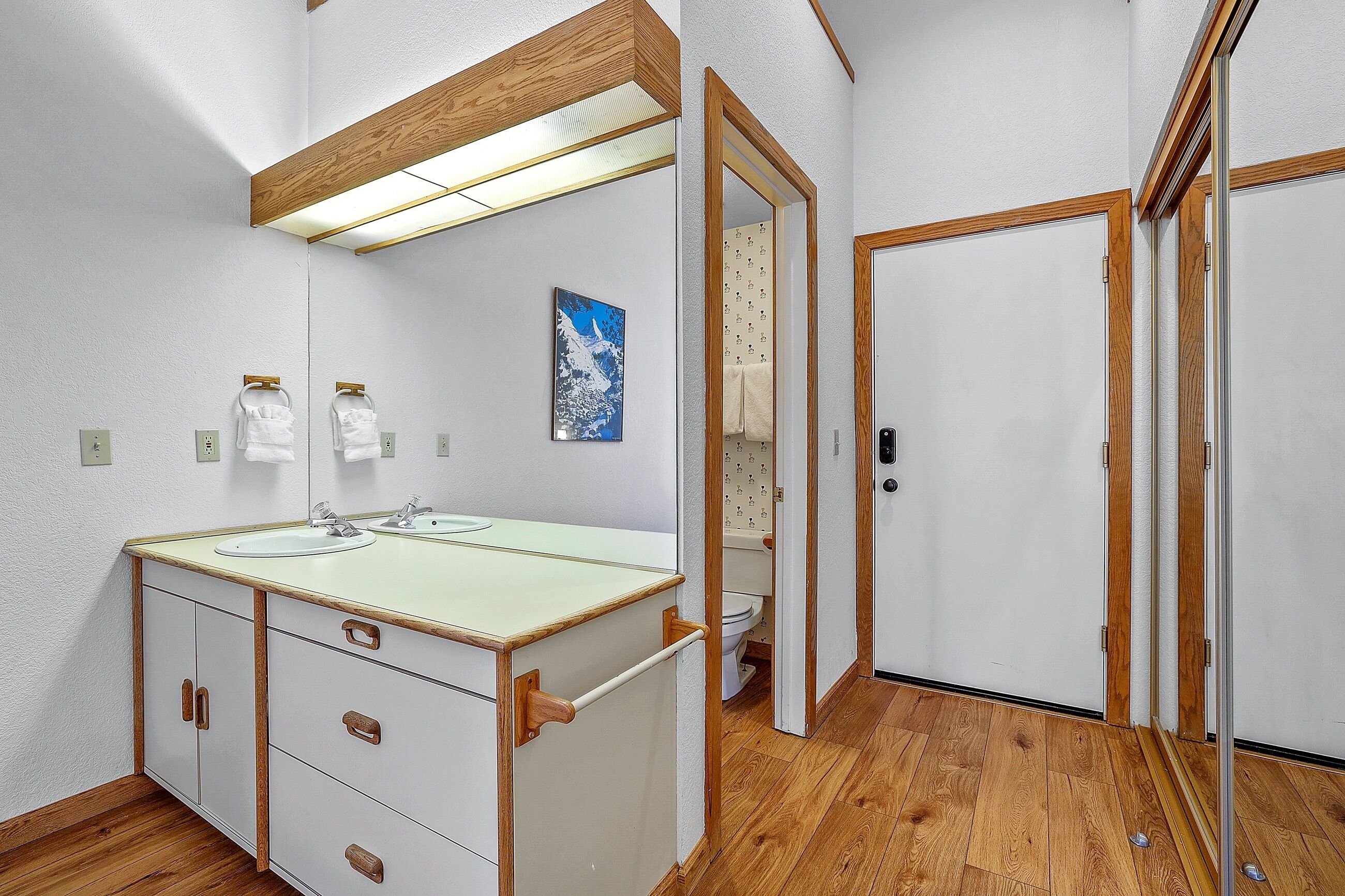 Un baño con tocador de madera, espejo, lavamanos e inodoro.