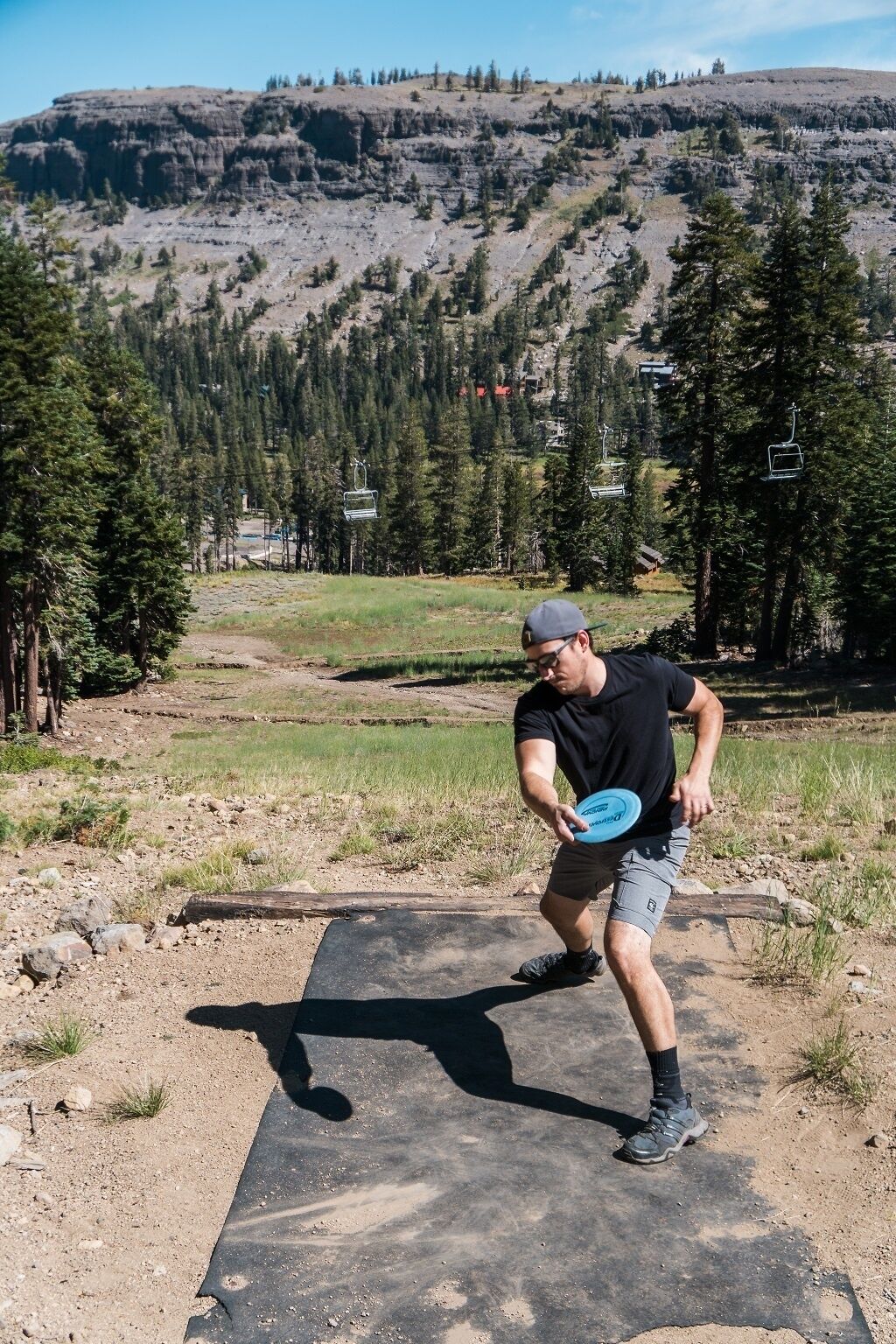 Une personne joue au frisbee dans un espace extérieur, avec un paysage montagneux en arrière-plan et des remontées mécaniques.