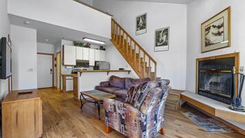 Una sala de estar con escalera de madera, chimenea y una cocina al fondo.