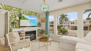 Ein Wohnzimmer mit Fernseher, Kamin, einer Couch und Blick auf Palmen.