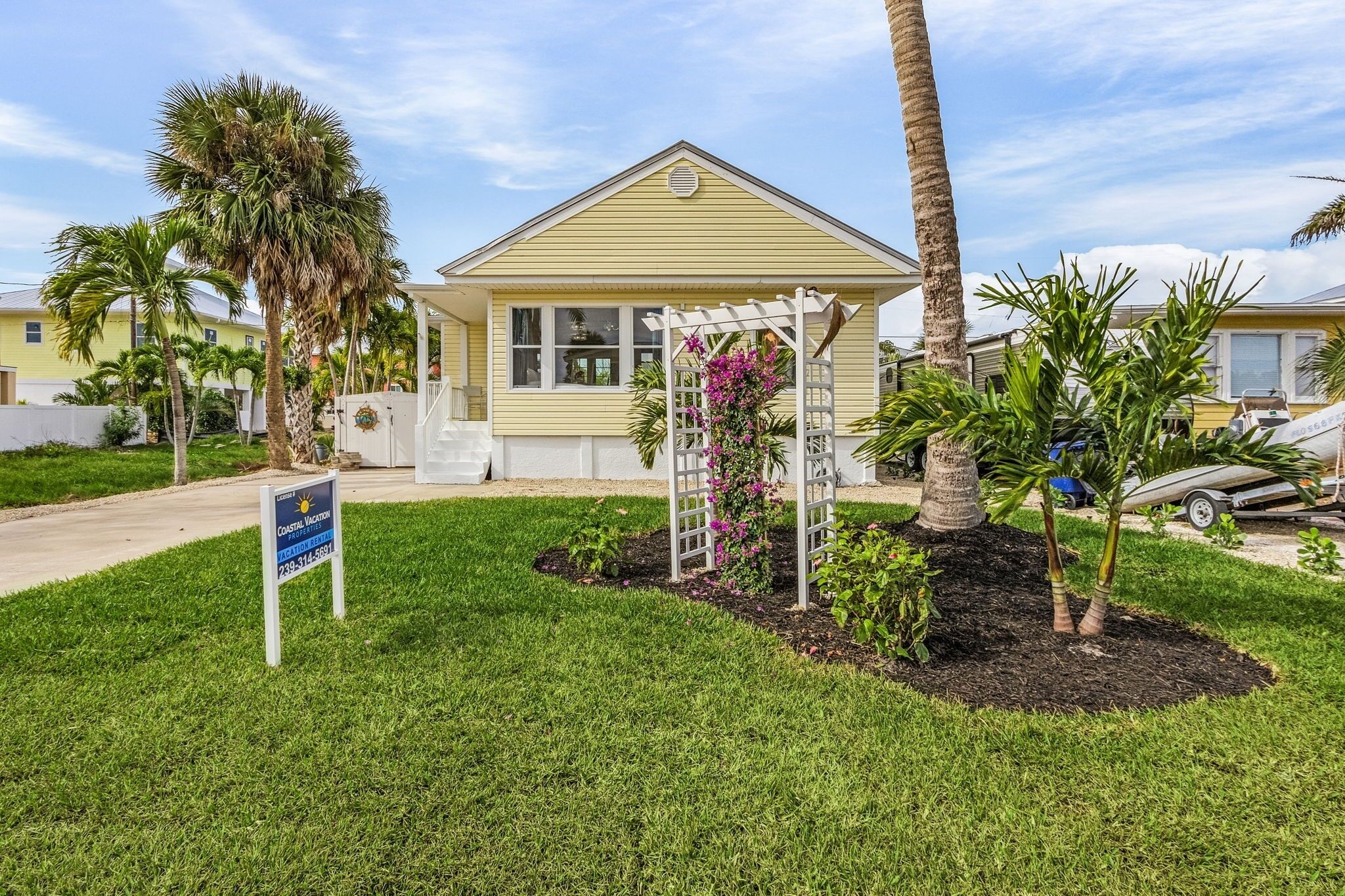 A single-story house with a white porch, surrounded by a well-maintained lawn and palm trees.