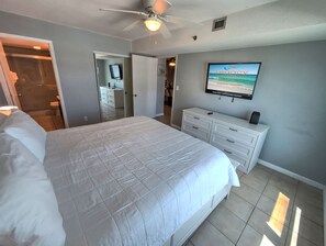 Un dormitorio con una cama grande, un ventilador de techo, un televisor en la pared y un aparador.