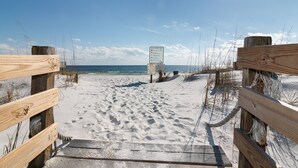 Ein hölzerner Steg führt zu einem Sandstrand, in der Ferne ist ein Schild zu sehen.