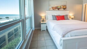 Ein Schlafzimmer mit großem Fenster, einem Bett, einem Nachttisch und einem Deckenventilator.