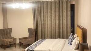 Ein Hotelzimmer mit einem großen Bett, zwei Sesseln, einem Schreibtisch und einer Deckenleuchte.
