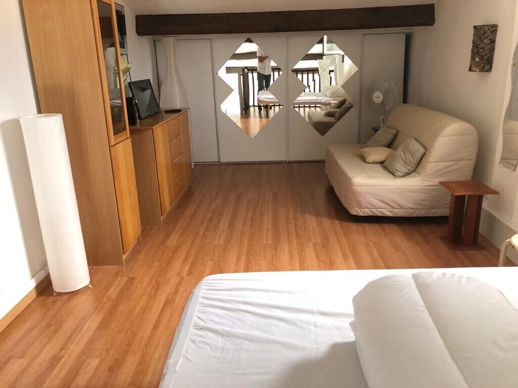 Un dormitorio con suelo de madera, una cama blanca, un sofá color beige y un armario con espejo.