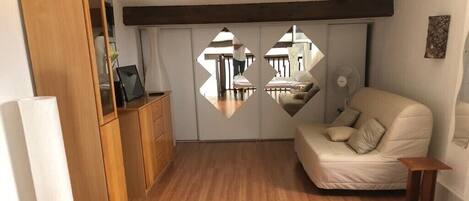 Un dormitorio con suelo de madera, una cama blanca, un sofá color beige y un armario con espejo.