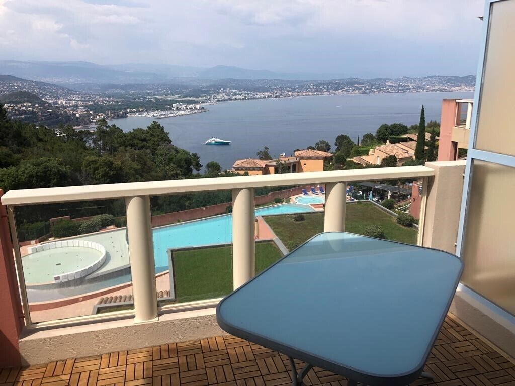 En balkon med udsigt over en swimmingpool, vand og fjerne bygninger.
