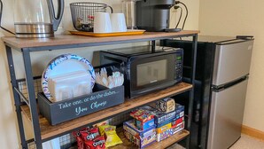 Une petite cuisine équipée d’une machine à café, d’un four à micro-ondes, d’une bouilloire et d’une étagère contenant des collations et de la vaisselle.