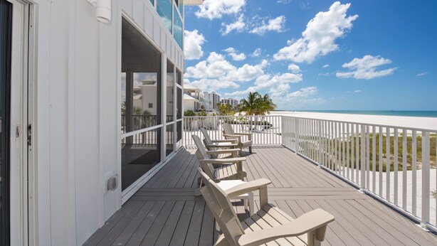 Een houten terras met lounge fauteuils en een balustrade, met uitzicht op een strand.