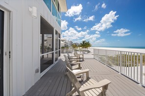Une terrasse en bois avec des chaises longues et une rambarde donnant sur une plage.
