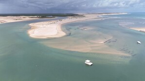 An aerial view of a coastal area with clear waters, sandy beaches, and a boat anchored near the shore. - Pousada & SPA Barra do Mundaú (Trairi)