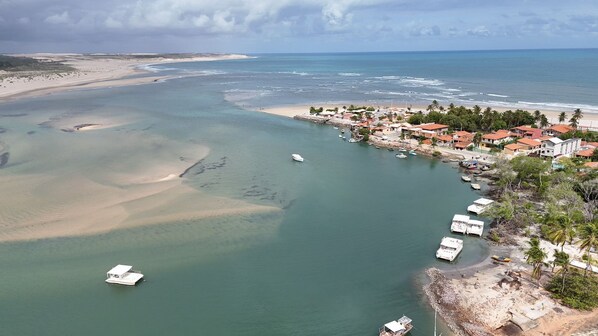 An aerial view of a coastal town with clear waters, boats, and buildings along the shore. - Pousada & SPA Barra do Mundaú (Trairi)