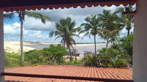 A view from a covered balcony with terracotta tiles, overlooking a beach with boats and palm trees. - Pousada & SPA Barra do Mundaú (Trairi)