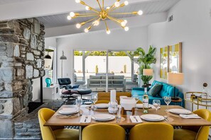 A dining area with a stone wall, a modern chandelier, and a view of the outdoors. - Starburst PS - Vibrant Mid-Mod Escape (Palm Springs)