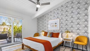 Une chambre à coucher comprenant un lit, deux chaises, une table de chevet, une lampe et un mur orné d’un motif géométrique.