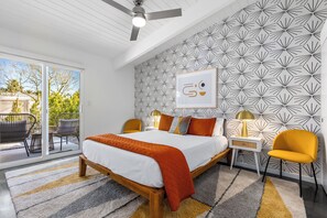A bedroom with a bed, two chairs, a nightstand, a lamp, and a wall with a geometric pattern. - Starburst PS - Vibrant Mid-Mod Escape (Palm Springs)