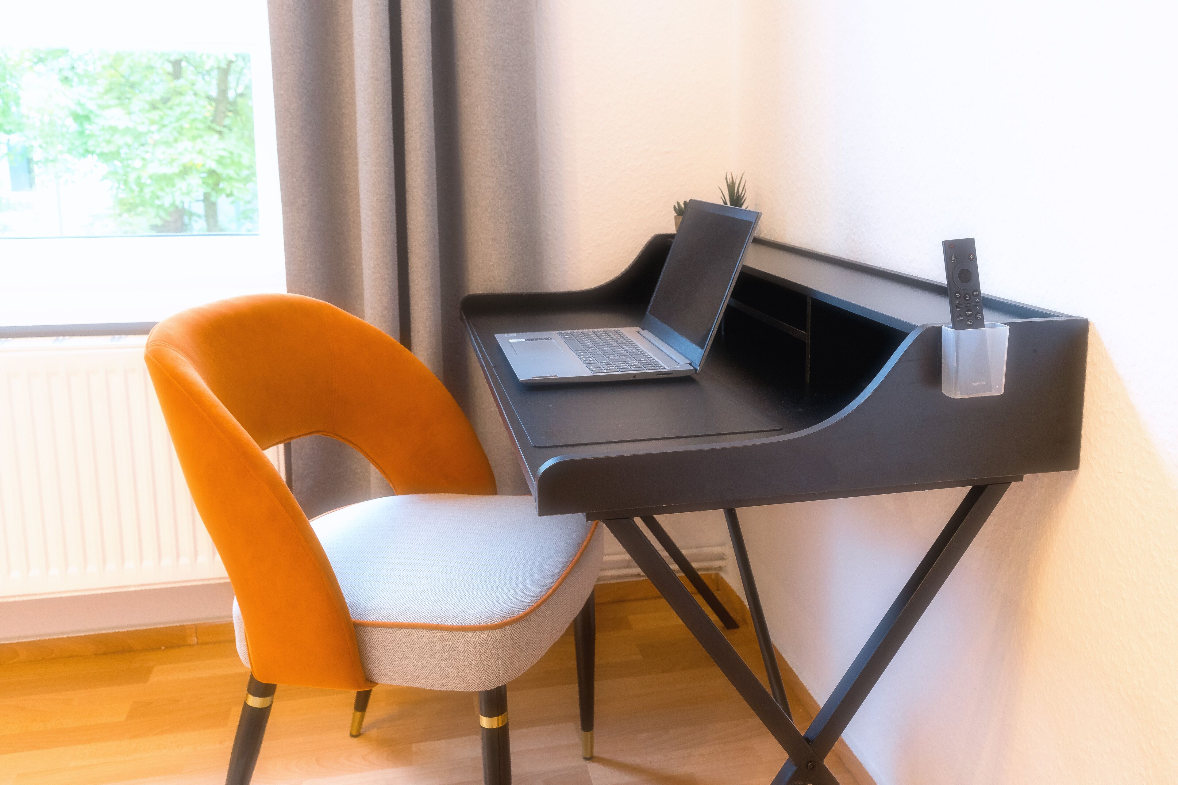 Un espace de travail moderne avec un ordinateur portable posé sur un bureau noir, une chaise et une télécommande.