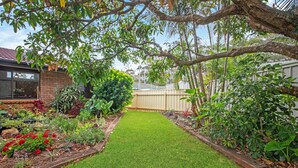 A well-maintained garden with a variety of plants and flowers, a neatly trimmed lawn, and a wooden fence. - 4 Shelly Beach Road: 2  BR, 2  BA House in Port Macquarie , Sleeps 4 (Port Macquarie)