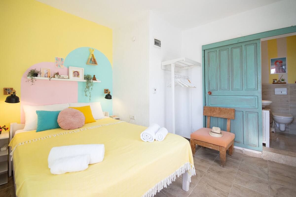A hotel room with a bed, a bench, a door, and a bathroom visible through an open door.
