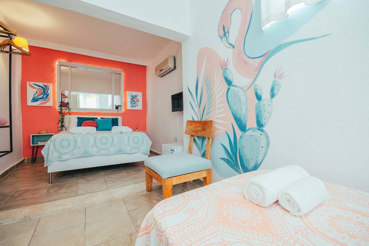 A bedroom with a bed, a bench, a wall mural, a window, and a bedside table.