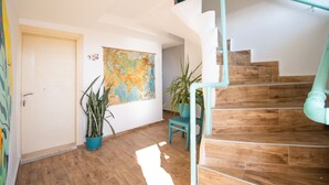 Un escalier avec des marches en bois et une rampe turquoise, menant à un palier où se trouvent une porte et une carte du monde accrochée au mur.