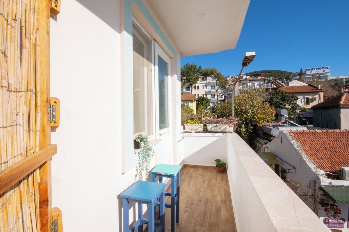A balcony with a wooden door, a small table, and a chair. There is a view of a building with a sign that reads "EKICI HOTEL".