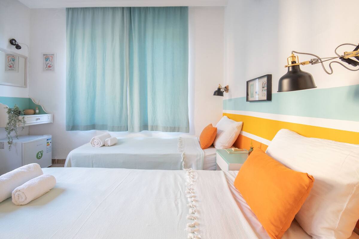 A hotel room with two beds, a desk, a desk lamp, and a window with curtains.