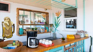 Une cuisine équipée d’une machine à café, d’un panier rempli de divers objets et d’un miroir accroché au mur.