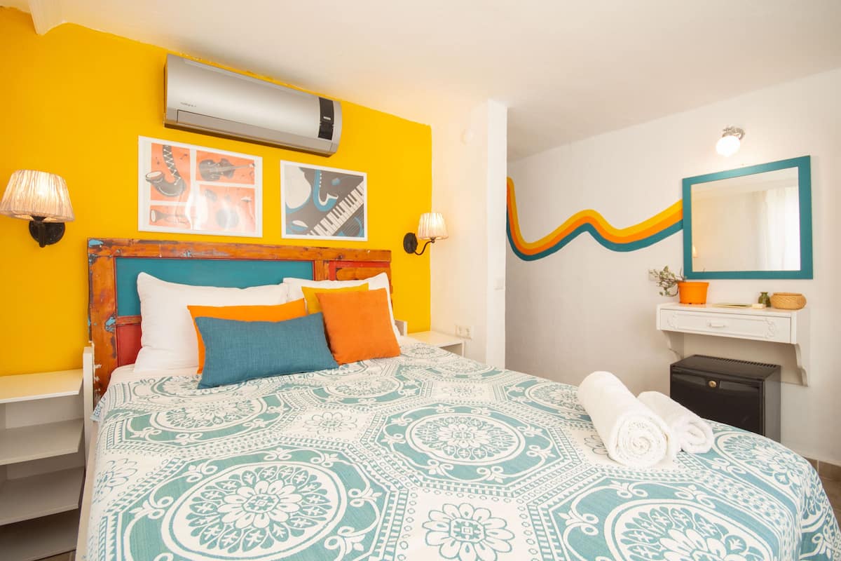 A hotel room with a bed, a nightstand, a wall-mounted air conditioner, a mirror, and a wall with a wavy design.