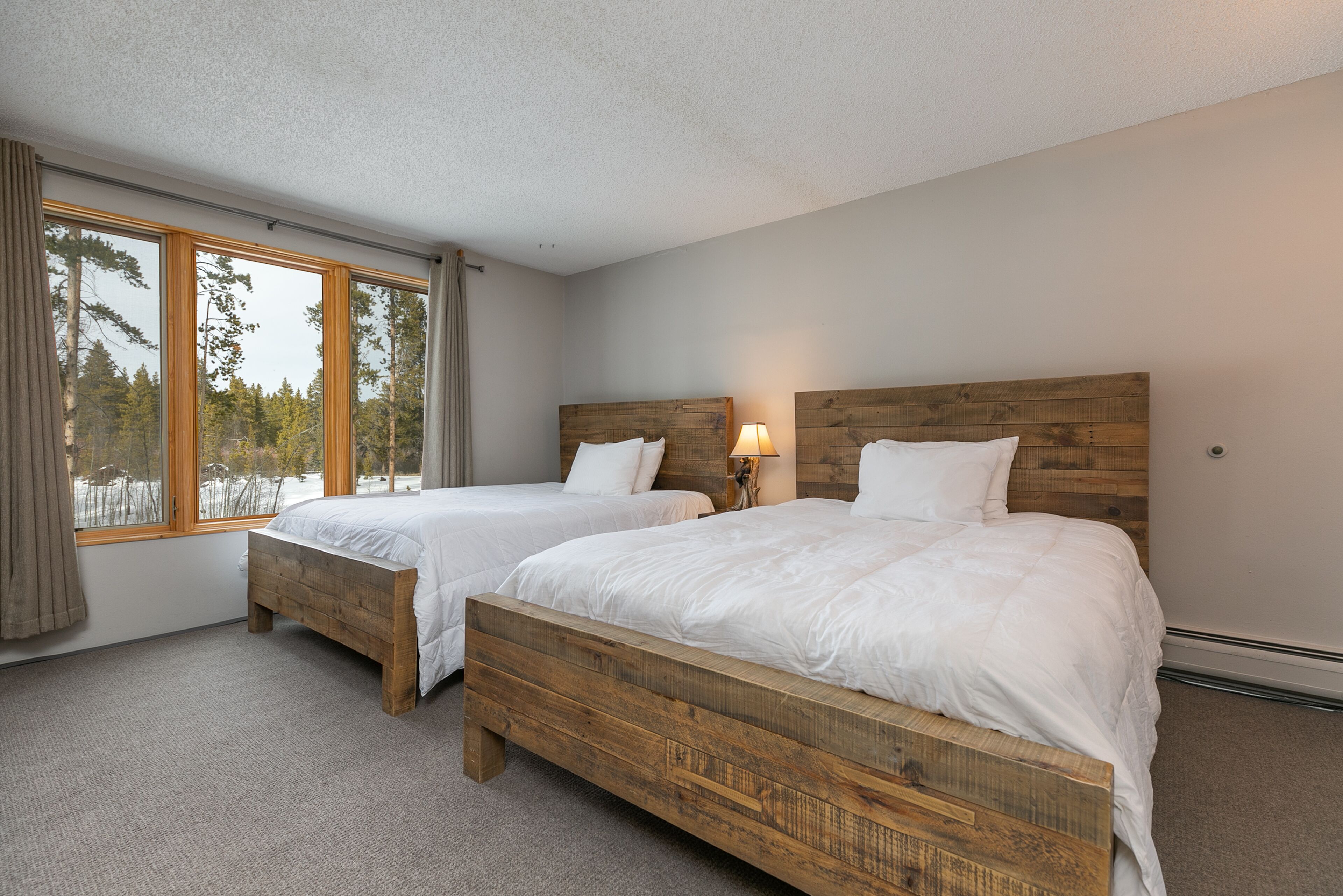 A bedroom with two wooden beds, a window with curtains, and a lamp on the nightstand.