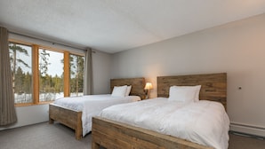 A bedroom with two wooden beds, a window with curtains, and a lamp on the nightstand.