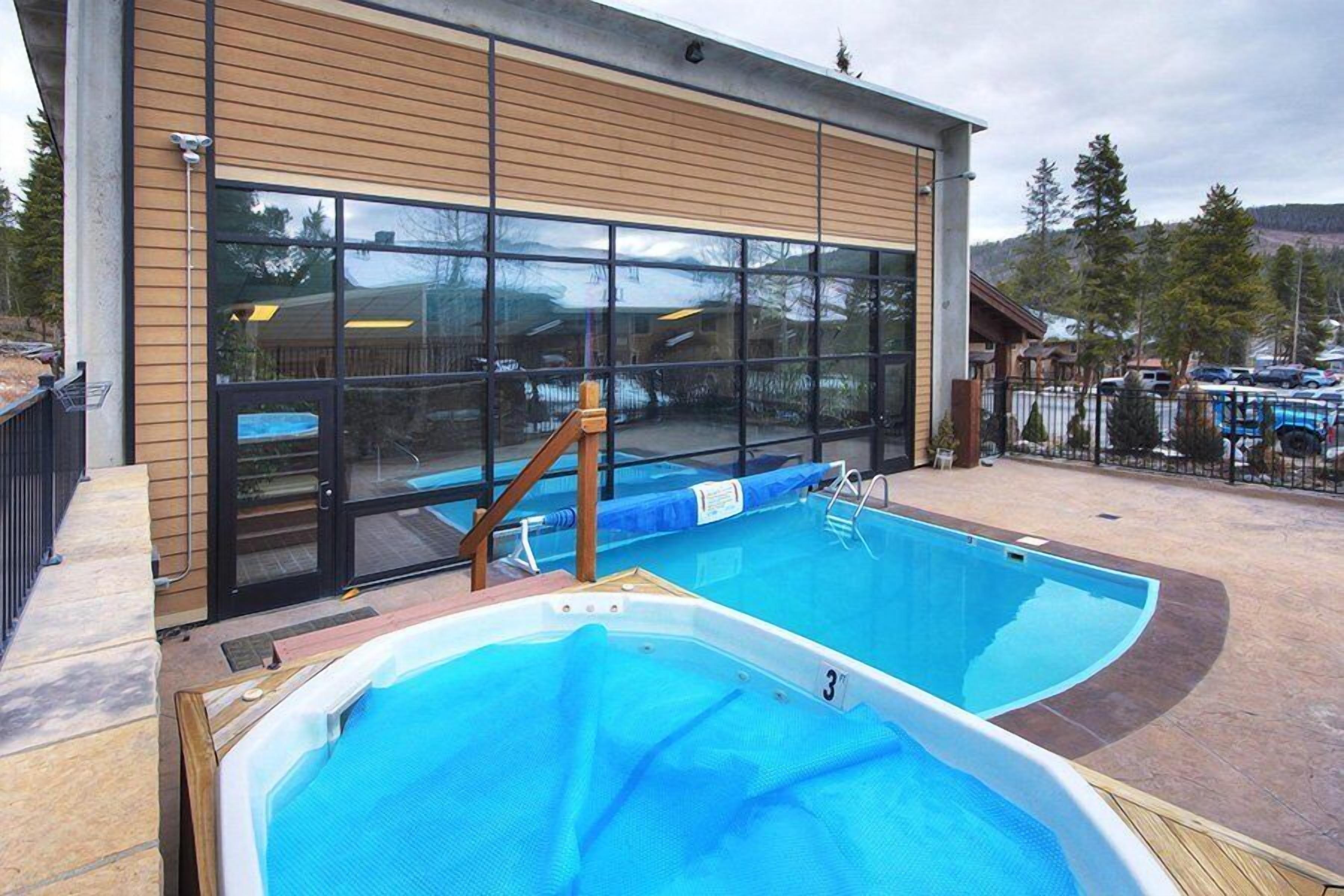 A pool area with a hot tub and a pool, adjacent to a building with large windows.