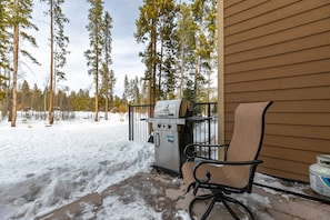 A covered grill area with a chair, a metal grill, and a wooden building in the background. - Claimjumper Retreat Townhome: Pool & Hot Tub, Walk to Town! (Breckenridge)