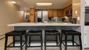 A modern kitchen with a central island, wooden cabinets, stainless steel appliances, and bar stools.
