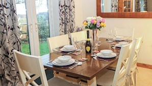 Mesa de comedor lista para seis personas, con sillas blancas, un jarrón de flores y una botella de vino.