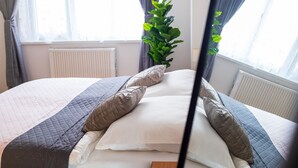 A neatly made bed with a quilted bedspread and pillows, a potted plant, and a window with curtains. - Central Cozy & Charming Residence 3min from Riverside Prague (Hlavní mesto Praha)