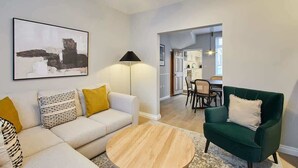 A modern living room with a sofa, a round coffee table, and a green armchair. There is a lamp and a painting on the wall.