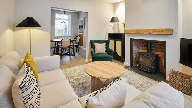 A modern living room with a sofa, a round coffee table, a fireplace, and a dining area in the background.
