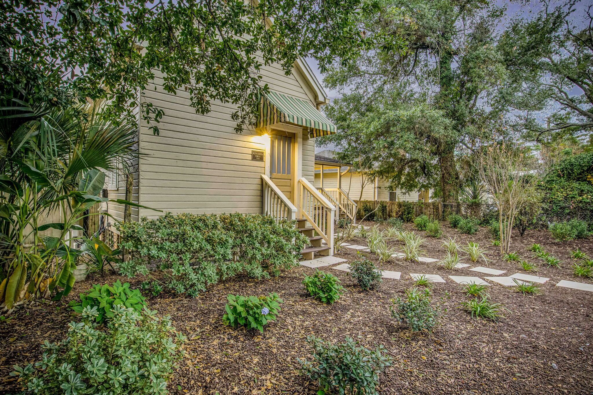 A house with a front porch, a staircase, and a garden with various plants and a stone pathway.