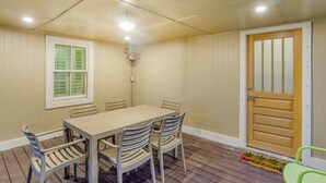 A room with a wooden floor, a table with chairs, a window with shutters, a door, and a ceiling fan.