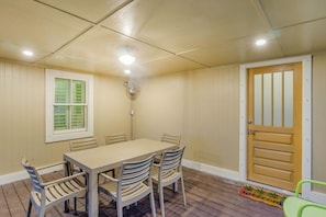 Una habitación con piso de madera, una mesa con sillas, una ventana con contraventanas, una puerta y un ventilador de techo.
