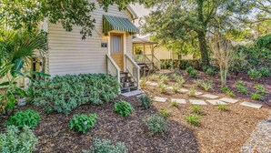 A house with a front porch, steps leading to the door, and a garden with various plants and a stone pathway.