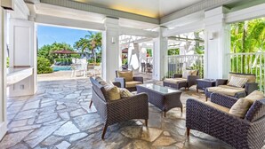 A covered outdoor seating area with wicker furniture and a stone floor, overlooking a pool and lush greenery. - The Islands M2 Oasis at Mauna Lani Resort (Kamuela)