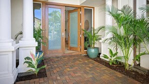 A brick pathway leading to a wooden door with glass panels, flanked by white columns and potted plants. - The Islands M2 Oasis at Mauna Lani Resort (Kamuela)